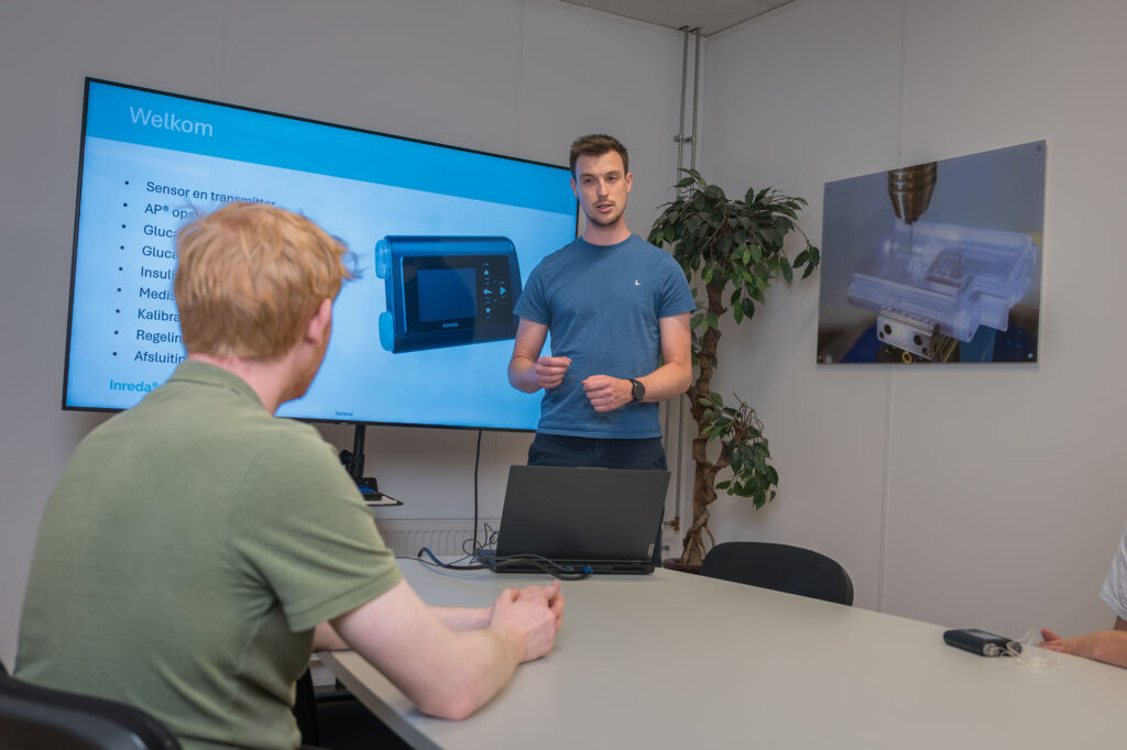 Twee collega’s overleggen in een vergaderruimte bij een scherm met een presentatie over de Inreda AP